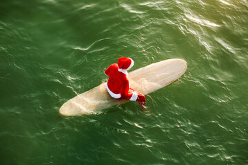 A man Dressed as Santa at the Beach with a surfboard