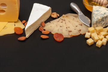 Different types of cheese on a wooden board decorated with honey, grapes, dried apricots and nuts