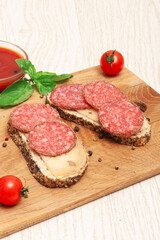 Sandwiches with smoked sausage and cheese on a wooden board decorated with cherry tomatoes and basil