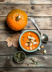 Pumpkin soup and pumpkin seeds in bowl with ripe pumpkin.