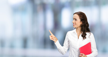 Profile portrait image of confident business woman with red folder, showing pointing finger, advertising, over blurred modern office background. Businesswoman, executive worker, teacher gesturing