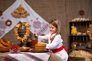 Little cheerful girl in national costume pouring tea from samovar while celebrating Maslenitsa. 