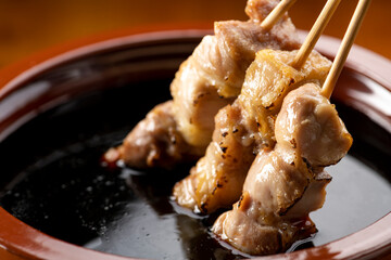鶏のモモ肉の串焼きをタレ壺の中の焼き鳥のタレに漬ける