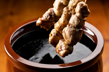 鶏のモモ肉の串焼きをタレ壺の中の焼き鳥のタレに漬ける