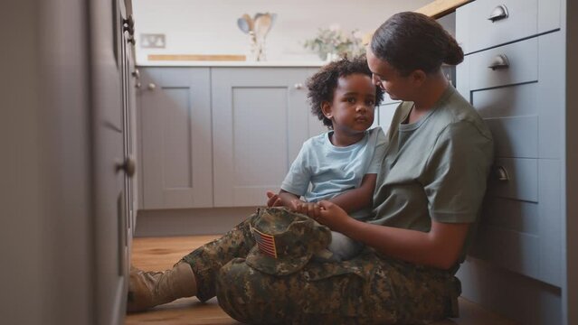 American Army Mother In Uniform Home On Leave Hugging Son Sitting On Floor In Family Kitchen