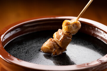 鶏のモモ肉の串焼きをタレ壺の中の焼き鳥のタレに漬ける