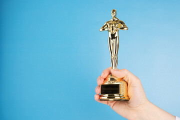 Oscar statue, award in hand on blue background,copy space - obrazy, fototapety, plakaty