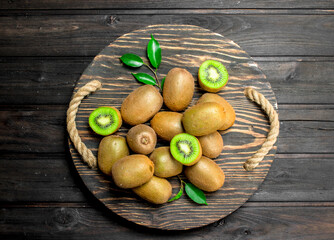 Ripe kiwi with leaves on a wooden tray.