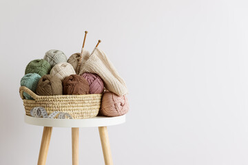 Natural wool in balls of various pastel colors in a wicker basket on table.