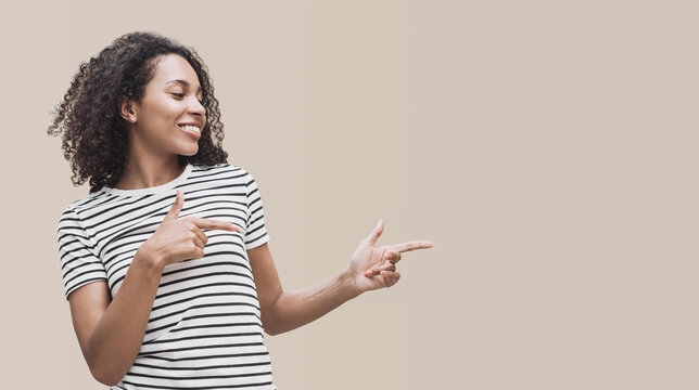 Beautiful black woman pointing to product isolated on beige background. Studio portrait of young girl showing way with fingers, advertisement concept