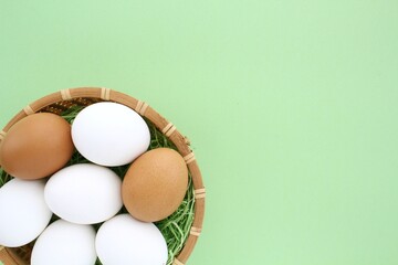 Fresh chicken eggs in wooden rattan wicker basket on green background. Natural healthy nutrition organic farm food product concept. World egg day, easter holiday composition. Close-up, flatlay