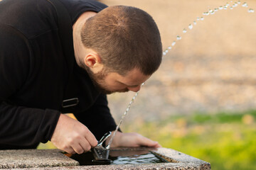 man drinking water from a drinking fountain in the park