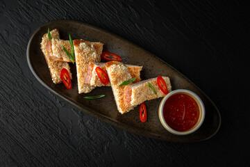 Shrimp toast in a ceramic plate on a dark textured background. Restaurant menu Isolated on black