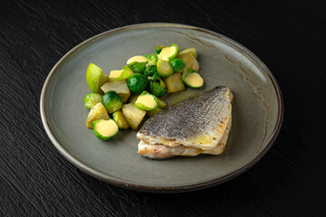 Dorada with artichoke and Brussels sprouts in a ceramic plate on a dark textured background. Restaurant menu Isolated on black