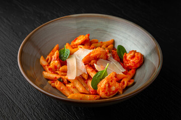 Penne with olives and shrimp in a ceramic plate on a dark textured background. Restaurant menu Isolated on black