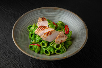 Creamy pasta with spinach and turkey in a ceramic plate on a dark textured background. Restaurant menu Isolated on black