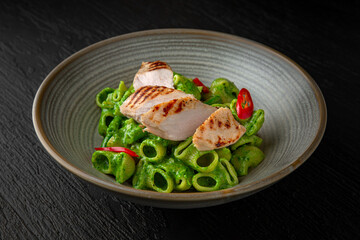 Creamy pasta with spinach and turkey in a ceramic plate on a dark textured background. Restaurant menu Isolated on black
