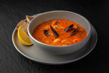 Seafood soup in a ceramic plate on a dark textured background. Restaurant menu Isolated on black