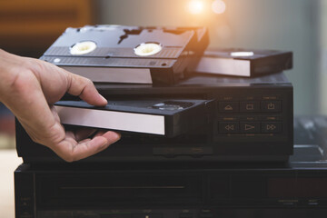 Close-up hand chooses and put or insert video cassette tape VHS on video tape player concept of vintage electric retro style and electronic appliances multimedia player device old fashioned.