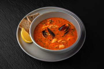 Seafood soup in a ceramic plate on a dark textured background. Restaurant menu Isolated on black