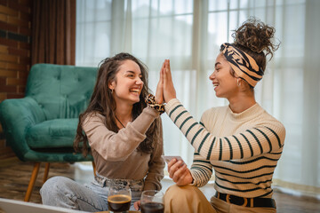 Two friends or girlfriends or sisters are high fiving and smiling because they made good purchase...