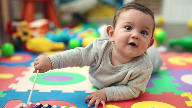 Adorable hispanic baby playing xylophone lying on floor at kindergarten