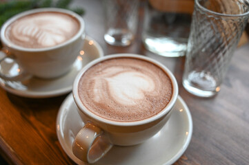 Close-up of a cup of hot latte coffee on the wooden table. Two white cups of cappuccino