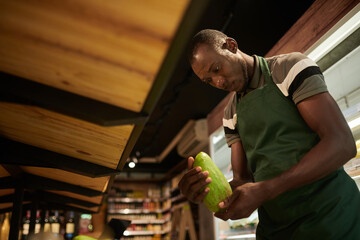 Supermarket worker putting green mangoes on shelf