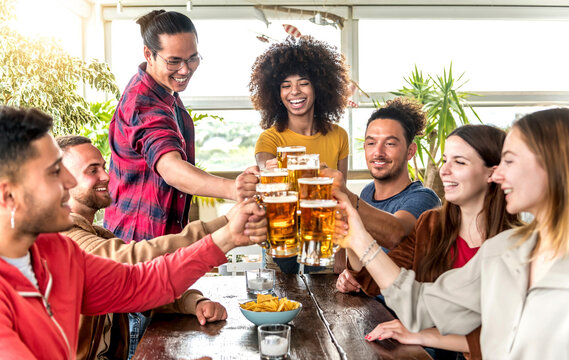 Multiracial group of happy friends enjoying a beer at brewery bar - Young people toasting and cheering aperitif beers half pint at happy hour at restaurant - Friendship and youth concept