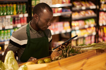 Grocery store worker with tablet computer checking if fruits on shelves got rotten