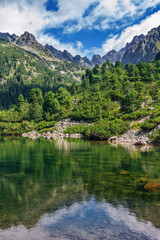 Naklejka na ściany i meble Beautiful summer landscape of High Tatras, Slovakia - Poprad lake, lush forest, rocks in pure water, mountains and white clouds on the sky