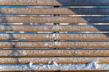 Wooden slats of the bench are covered with snow