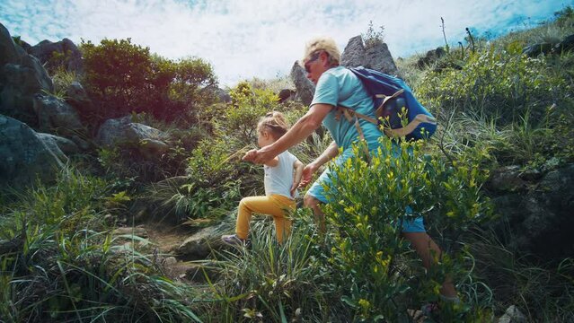 Family hiking. Elderly woman helps kid to pass difficult part of the hiking trail