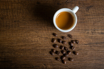 White cup of espresso with coffee beans on wooden table