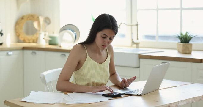 Busy young woman pays utility bills through on-line internet bank application using laptop check taxes, summarize on calculator, planning domestic family budget, do financial paperwork at home office
