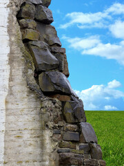 Close-up of stones of a broken wall, to an open blue sky and a green wide field.