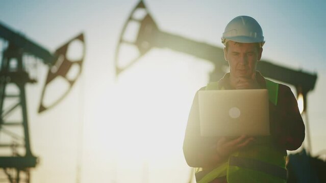 oil worker. engineer next to an oil rig. oil business production concept. gas production. a worker with a laptop monitors oil production next to an station. industry worker in hard hat works finance