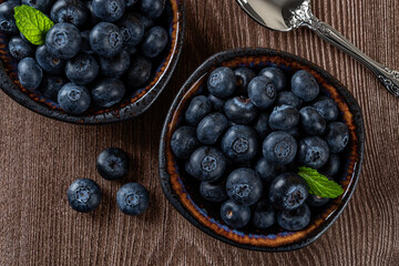 Ripe blueberries in a bowl over wooden background. Ready to eat healthy fruit dessert of wild berries. Tasty fresh blueberry as natural antioxidant. Vegan and vegetarian concept.