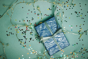 Beautifully wrapped in a violet box with a bow present among glowing LED garlands shining lights on blue background. Glowing illumination for New Year. Decor for celebration Christmas. Copy space.