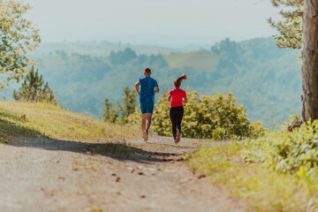 Fototapeta premium Couple enjoying in a healthy lifestyle while jogging on a country road through the beautiful sunny forest, exercise and fitness concept