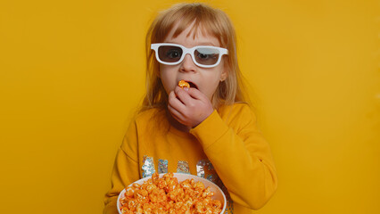 Excited young toddler school girl in 3D glasses eating popcorn, watching interesting tv serial,...