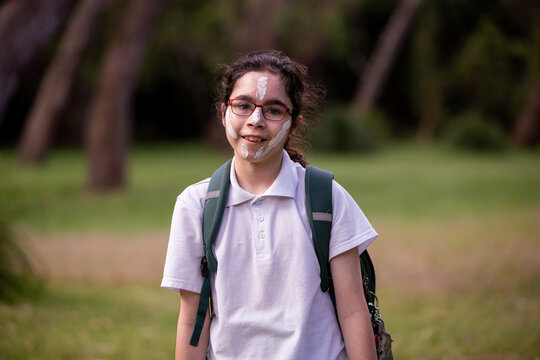 Young Aboriginal girl wearing a backpack, white face paint and glasses smiling at the camera