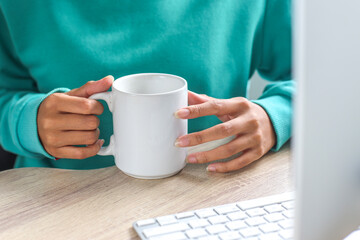 Hand of woman wearing tosca sweater holding white mug for mock up at office desk 
