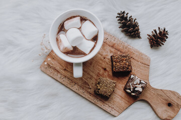 A cup of hot chocolate and marshmallow with brownie on wooden tray. 