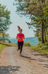 Young happy woman enjoying in a healthy lifestyle while jogging on a country road through the beautiful sunny forest, exercise and fitness concept