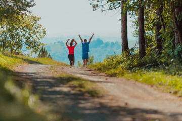 Obraz premium Couple enjoying in a healthy lifestyle while jogging on a country road through the beautiful sunny forest, exercise and fitness concept