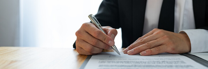 Young Asian legal advisor or lawyer reading financial details investment agreement Signing a contract for validity before the delivery of documents to help his clients succeed.