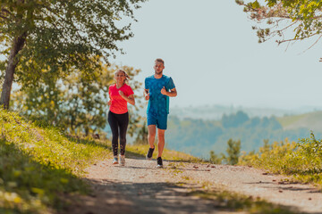 Couple enjoying in a healthy lifestyle while jogging on a country road through the beautiful sunny forest, exercise and fitness concept