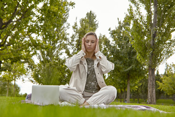 A woman sits cross-legged in the lotus position Sukhasana and meditates in the park. Attractive woman relieves stress by meditating in the park