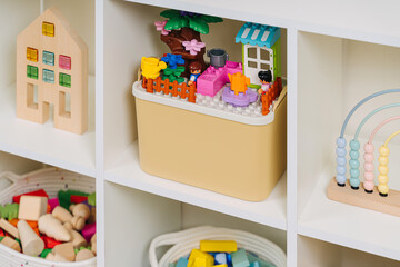 Naklejka premium White shelving with rainbow wooden toys and constructor pieces in storage baskets and boxes. Organizing and storage ideas in nursery.